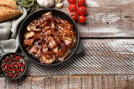 Delicious bacon slices in frying pan and products on wooden table, flat lay. Space for textの写真素材