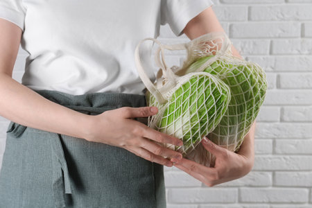 Woman holding string bag with fresh Chinese cabbages near white brick wall, closeupの写真素材