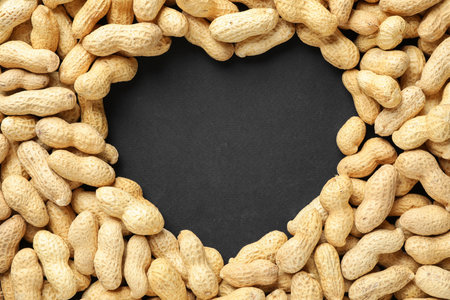 Heart made of unpeeled peanuts on black background, top view. Space for text