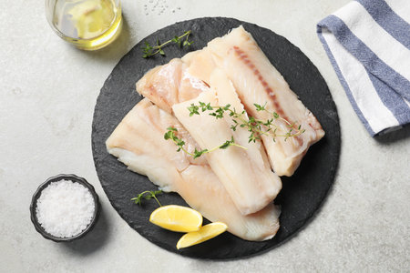 Pieces of raw cod fish, lemon, salt and oil on light gray table, top view