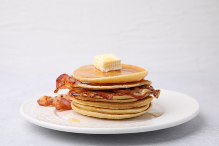 Delicious pancakes with bacon, butter and honey on light table, closeup