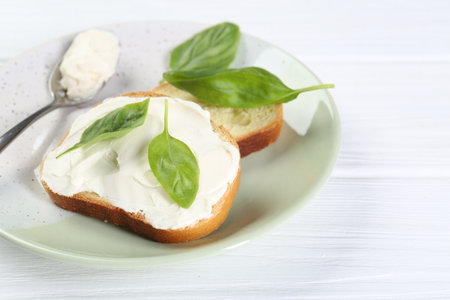 Pieces of bread with cream cheese and basil leaves on white wooden table. Space for textの写真素材
