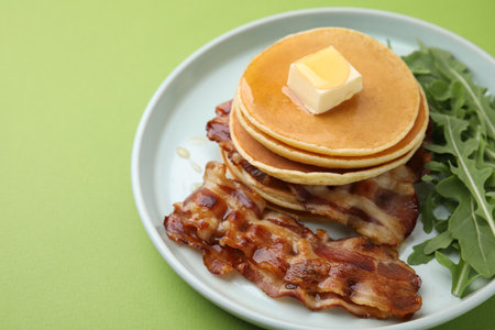 Tasty pancakes with butter, fried bacon and fresh arugula on light green backgroundの写真素材
