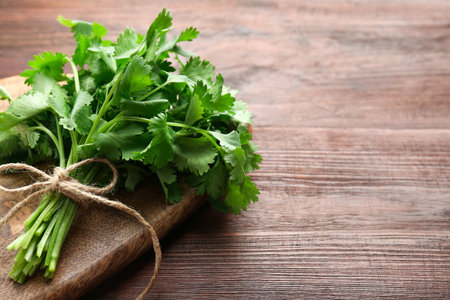 Bunch of fresh coriander on wooden table, space for text