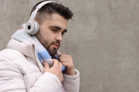 Handsome man in warm scarf and headphones near wall outdoors. Space for textの写真素材