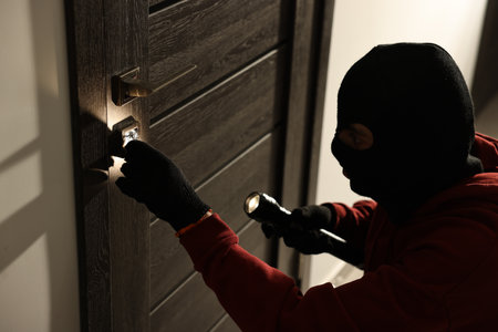 Thief with flashlight breaking foreign door's lock in hall. Burglaryの写真素材