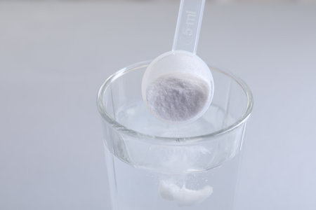 Adding baking soda into glass of water on light gray background, closeup