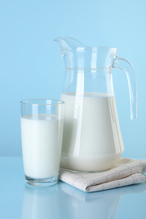 Jug and glass of fresh milk on light blue backgroundの写真素材