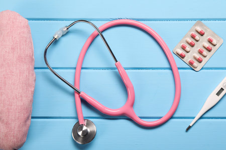 Pillow, stethoscope, thermometer and pills on light blue wooden background, flat layの写真素材