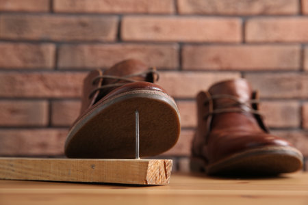 Metal nail in wooden plank and shoes on tableの写真素材