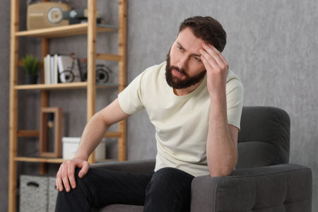 Overwhelmed man sitting in armchair at homeの写真素材