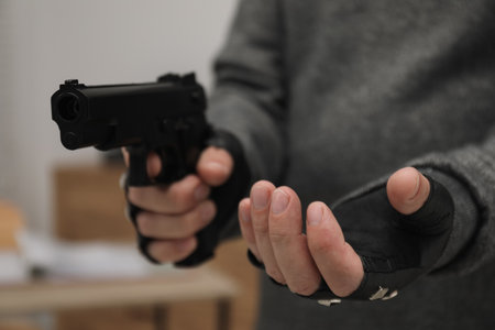 Dangerous criminal with gun indoors, closeup. Armed robbery