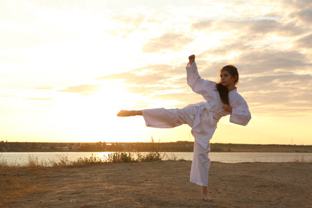Cute little girl in kimono practicing karate near river at sunsetの写真素材