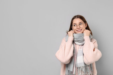 Beautiful woman in warm scarf and glasses on gray background, space for textの写真素材