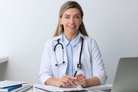Portrait of happy doctor with stethoscope at white table in hospitalの写真素材