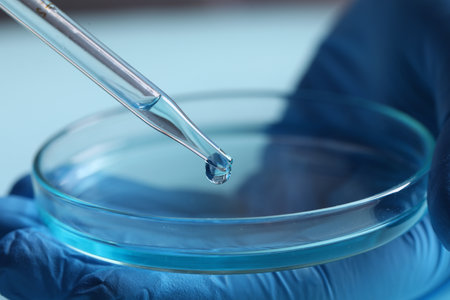 Doctor dripping liquid from pipette into petri dish on blurred background, closeup. Laboratory analysisの写真素材