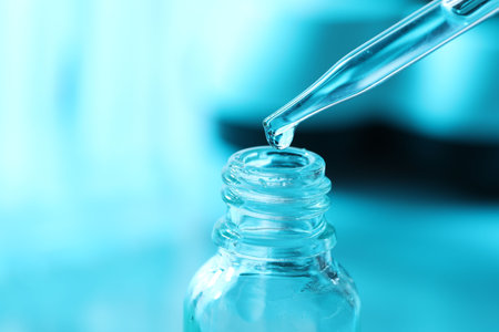 Dripping liquid from pipette into glass bottle on light blue background, closeupの写真素材