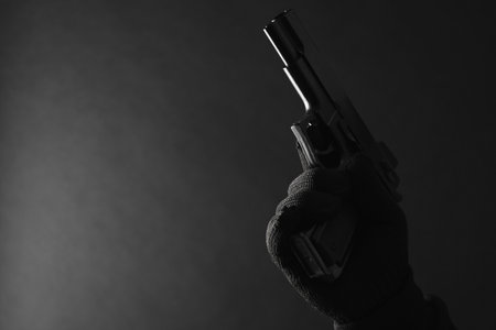 Armed robbery. Dangerous criminal with gun on black background, closeup. Space for textの写真素材