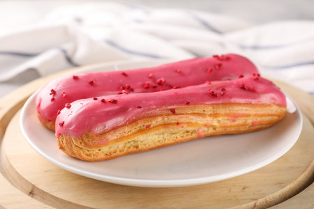 Plate with tasty glazed eclairs on wooden board, closeup