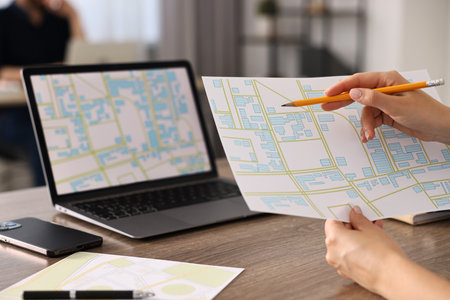 Cartographer working with cadastral maps at wooden table in office, closeup