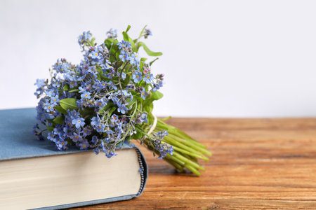 Bouquet of beautiful forget-me-not flowers and book on wooden table against light background, space for textの写真素材