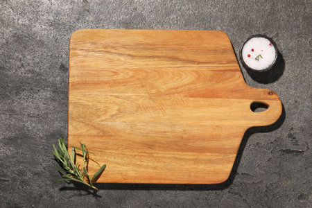 Wooden cutting board and spices on gray textured table, flat lay. Space for text