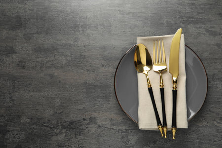 Elegant setting with golden cutlery on dark gray table, top view. Space for text