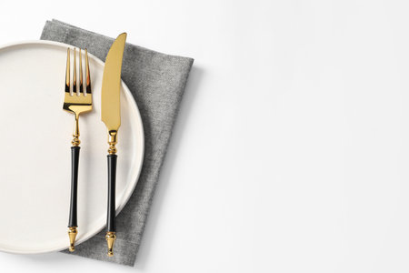Stylish golden cutlery, plate and napkin on white background, top view. Space for textの写真素材