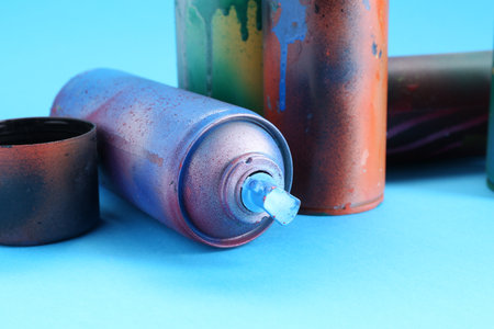 Spray paint cans and caps on light blue background, closeup