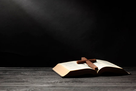 Bible and cross on gray wooden table against dark background, space for text. Religion of Christianityの写真素材