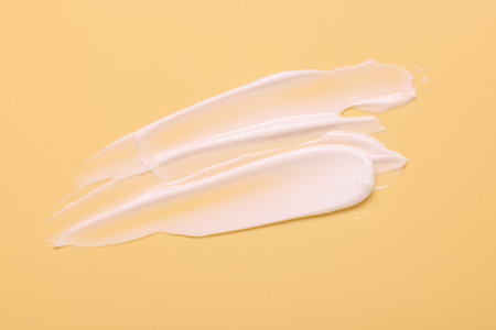 Samples of face cream on pale yellow background, top view