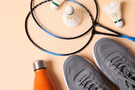 Feather badminton shuttlecocks, sneakers and bottle on beige background, flat lay