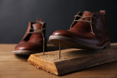 Metal nails in wooden plank and shoes on tableの写真素材