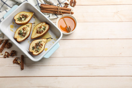 Tasty baked pears with nuts, blue cheese, thyme and honey in baking dish on wooden table, flat lay. Space for textの写真素材
