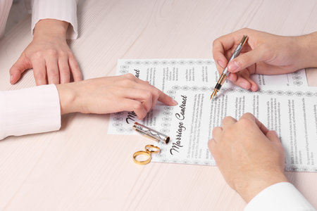 Man and woman signing marriage contract at light wooden table, closeupの写真素材