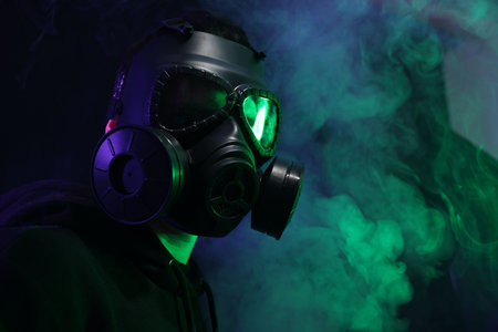 Man wearing gas mask in color lights and smoke on black background. Space for textの写真素材