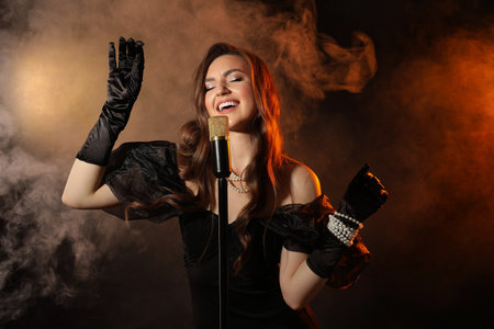 Beautiful young woman with microphone singing in color lights and smoke