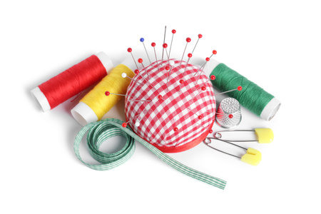Checkered pincushion with sewing pins, spools of threads, ribbon and thimble isolated on white, above viewの写真素材