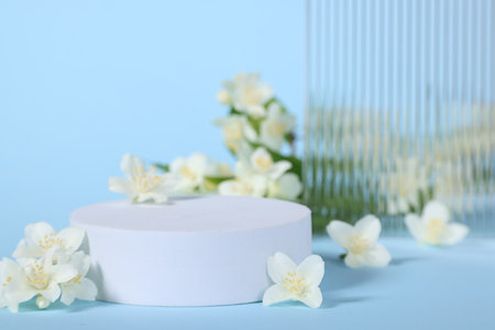 Presentation of product. White podium and beautiful jasmine flowers on light blue background, closeupの写真素材
