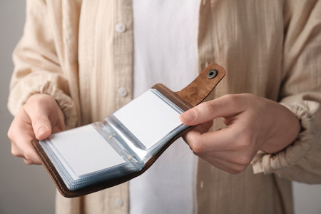 Woman holding leather business card holder with blank cards on gray background, closeup