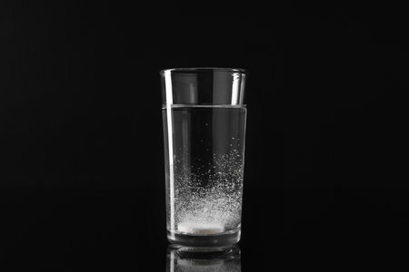 Effervescent pill dissolving in glass of water on black backgroundの写真素材