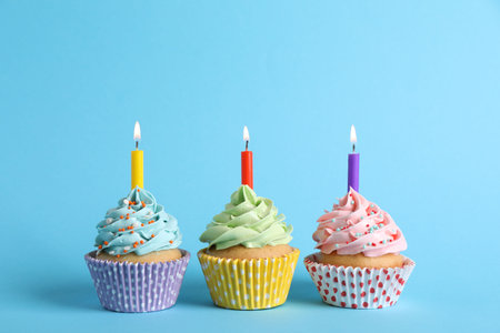 Birthday cupcakes with burning candles on light blue backgroundの写真素材