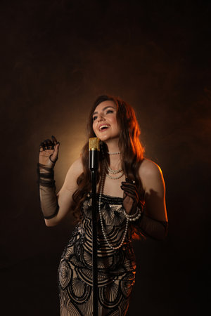 Beautiful young woman in stylish dress with microphone singing on dark background with smoke