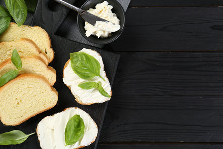 Pieces of bread with cream cheese and basil served on black wooden table, flat lay. Space for textの写真素材