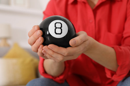 Woman holding magic eight ball indoors, closeup