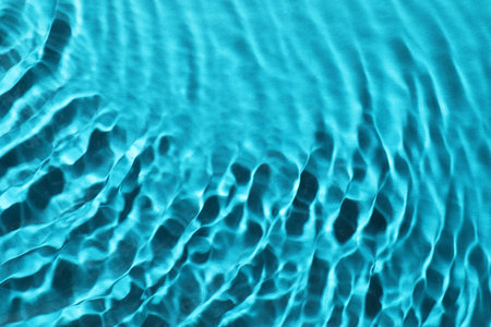 Rippled surface of clear water on light blue background, closeup