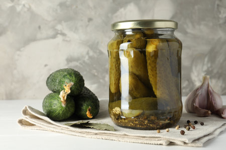 Pickles in jar, fresh cucumbers and spices on white tableの写真素材