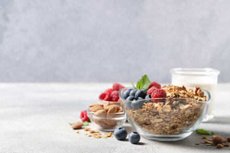 Tasty granola with berries, nuts and mint on gray table. Space for text