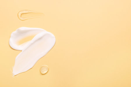 Samples of face cream on pale yellow background, top view. Space for text