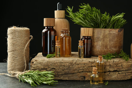 Essential oils in bottles, rosemary, thread and wood on gray table against black backgroundの写真素材